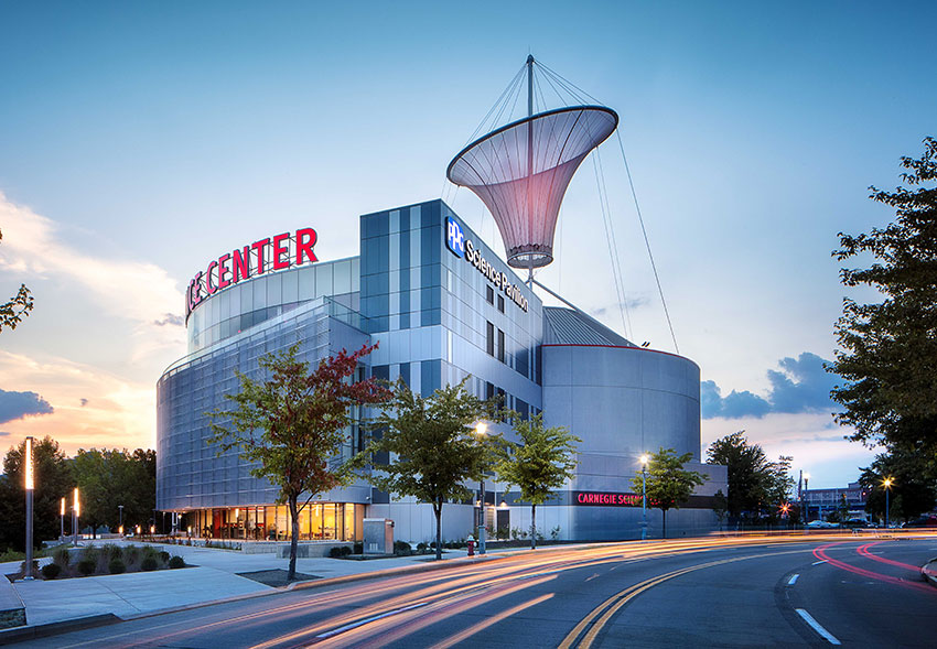 The Carnegie Science Center, featuring modern architecture and a large, striking cone-shaped structure on top, at dusk with street lights.