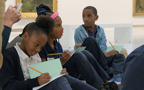 Children sitting on the floor in an art gallery, engaged in creative activities with sketchbooks and pencils.