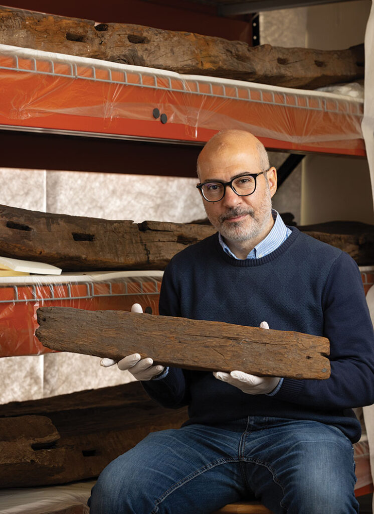 A man posing while holding a piece of wood from an ancient Egyptian boat.