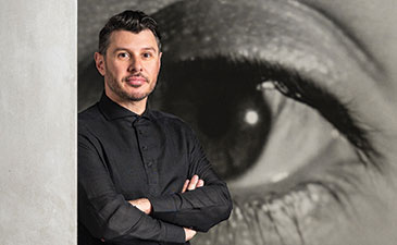 A portrait of Aaron Garvey with a large photo of a human eye behind him.