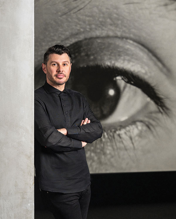 A portrait of Aaron Garvey with a large photo of a human eye behind him.