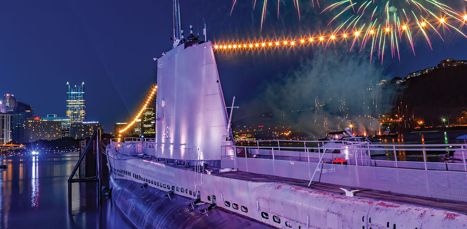 A dramatic photo of a submarine at night with lights and fireworks around it.