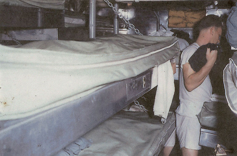 a vintage photo of a crew member on a submarine next to his bunk.