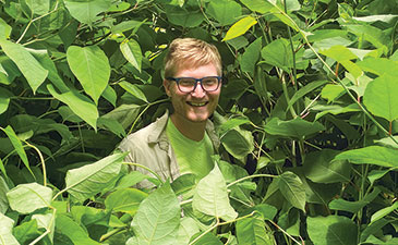 man surrounded by green plants with only his face visible.