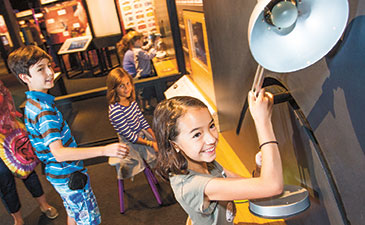 A group of children exploring an exhibit of a lamp.