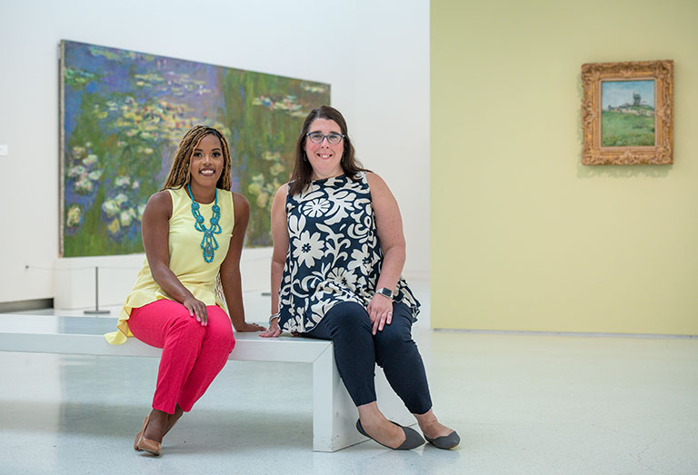 Two young female educators sitting on a bench in an art museum gallery.