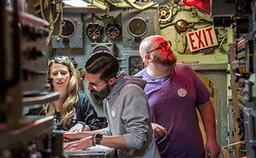 Three people working together at a table inside of a submarine.