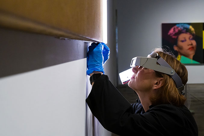 A museum conservator, wearing eyewear, working on a piece of artwork