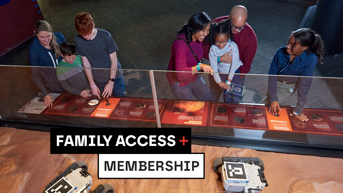 A family explores interactive exhibits at a science center, with a robot on display and educational panels detailing space exploration.