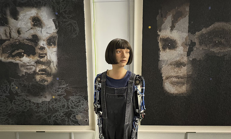 A humanoid robot stands between two abstract portraits, resembling faces, showcasing a blend of art and technology in an exhibition space.
