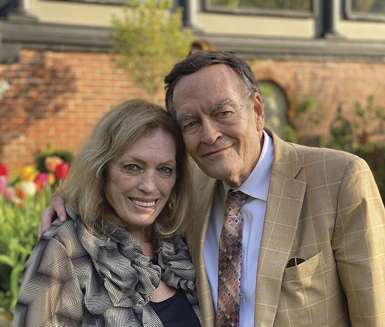 A couple poses together in a garden, surrounded by colorful tulips, with a picturesque brick wall and greenery in the background.