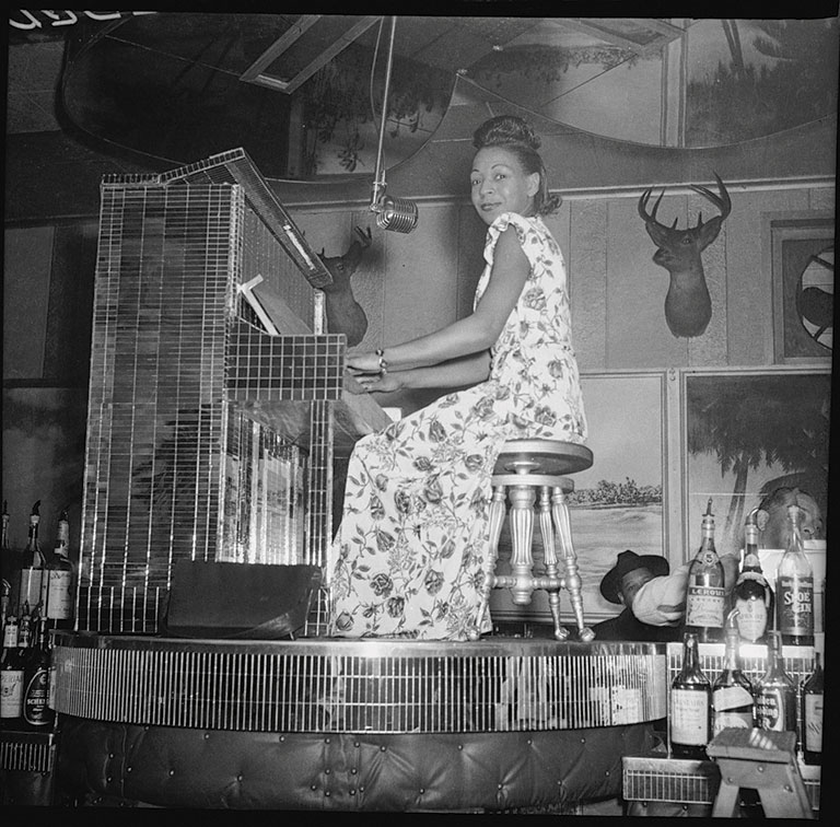 A musician plays a vintage piano on a stage surrounded by bottles and deer heads on the wall, creating a lively atmosphere.