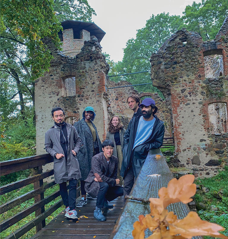 A group of people standing on a wooden bridge leading to the ruins of a castle.