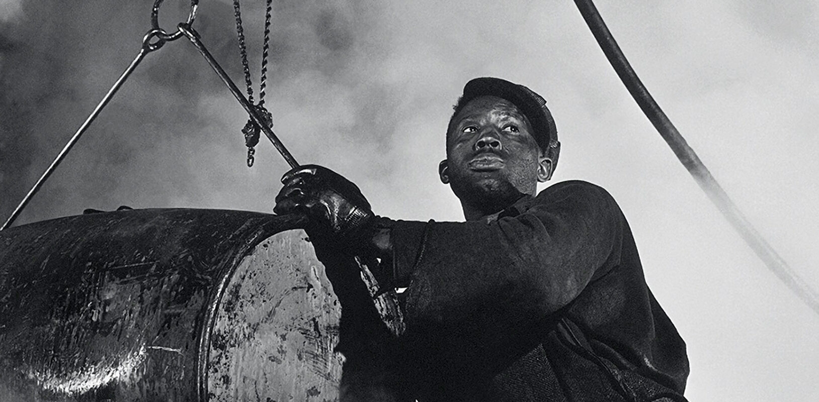 a man looks into the distance while handling a large vat of grease.