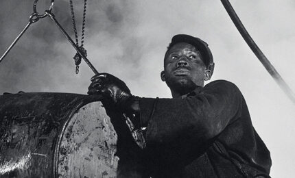 a man looks into the distance while handling a large vat of grease.