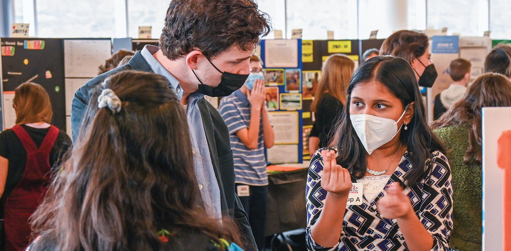 A young firl at a science fair talking to an adult