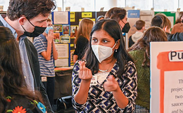 A young firl at a science fair talking to an adult