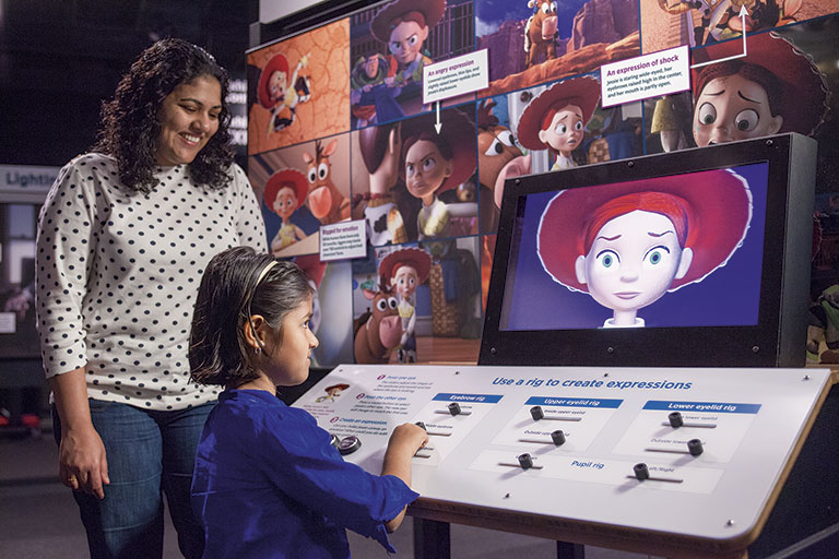 A young girl and her mother at an interactive exhibit in the Pixar exhibition.