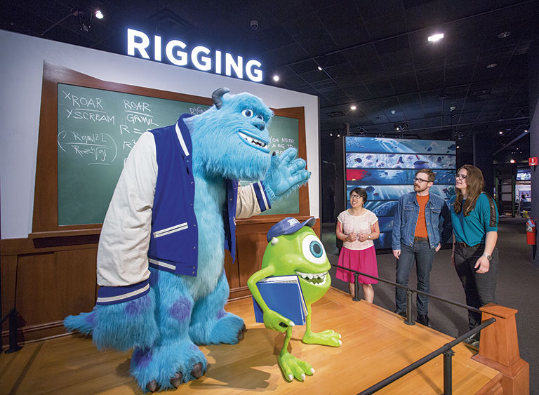 Three people looking at a display of two Pixar characters. The word Rigging is above the display.