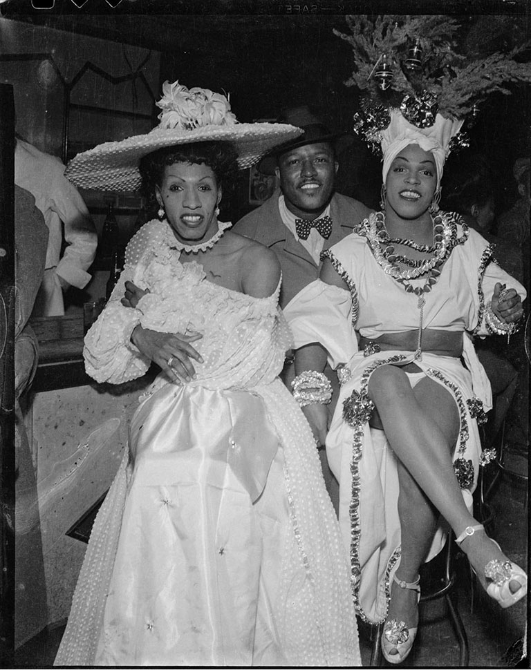 A black and white photo of a man sitting between two cross-dressers.