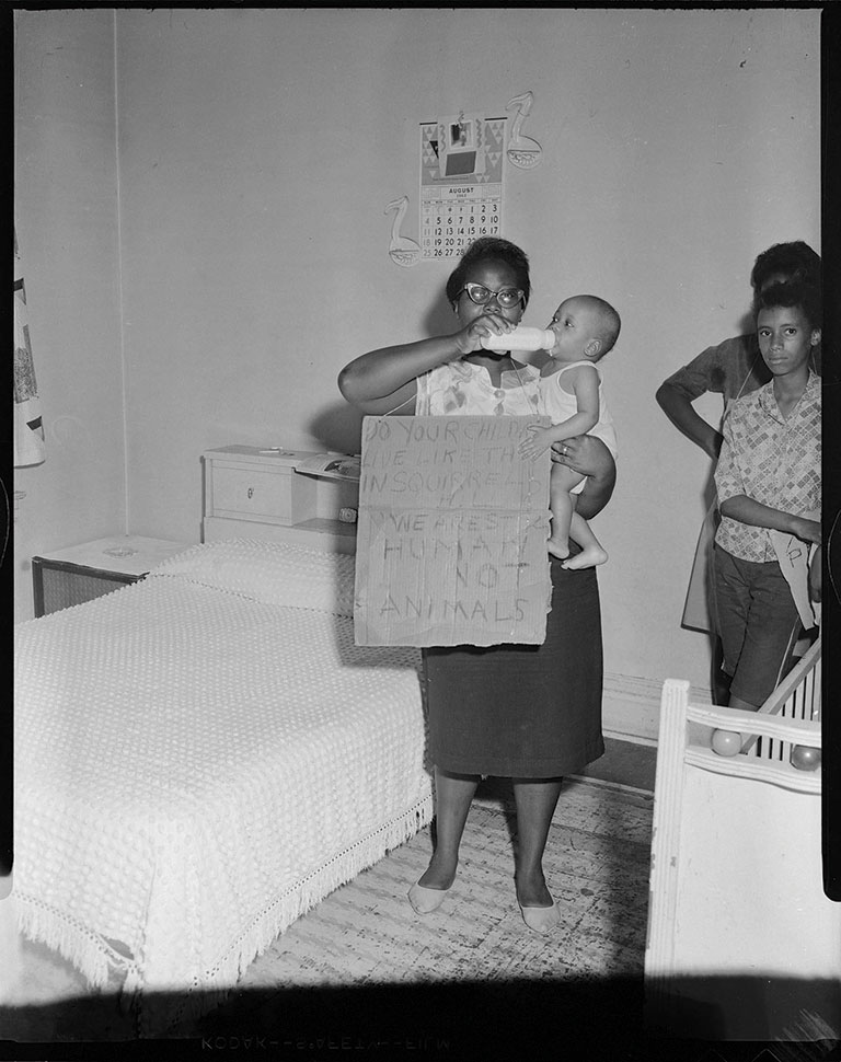 A 1963 photo of a woman holding a baby and a cardboard sign.