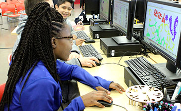 A young girl in a blue shirt working on a computer.