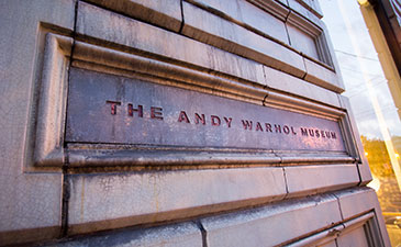 Close-up of the entrance sign for The Andy Warhol Museum, featuring textured stone and bold red lettering.