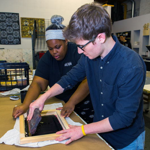 two people working on a adding ink to a silkscreen