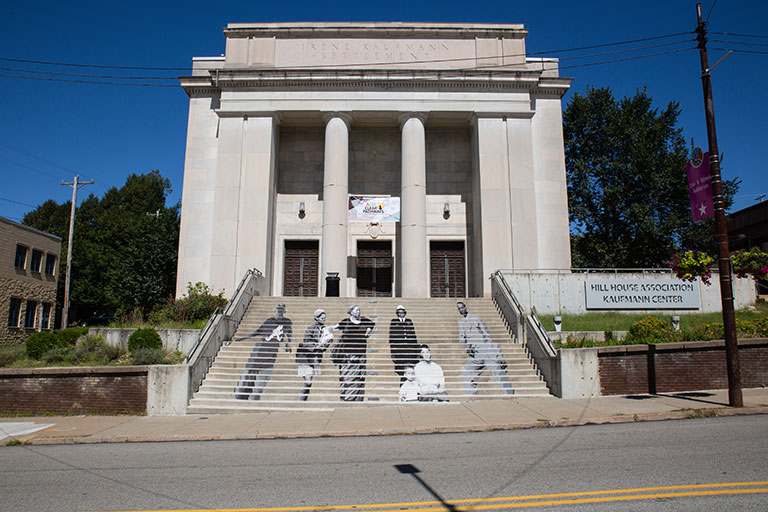 The exterior of a building with a mural of people painted on teh steps leading to the door.