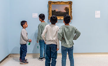 Four young boys stand in an art gallery, gazing at a painting framed on the wall, set against a light blue background.