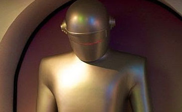 A shiny, humanoid robot stands in a curved alcove, featuring a smooth metallic surface and a simple, helmet-like head.