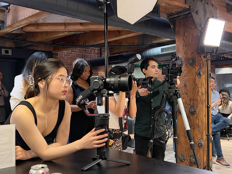 A group of photographers at an event, one woman operating a camera while others prepare equipment in a stylish, rustic space.